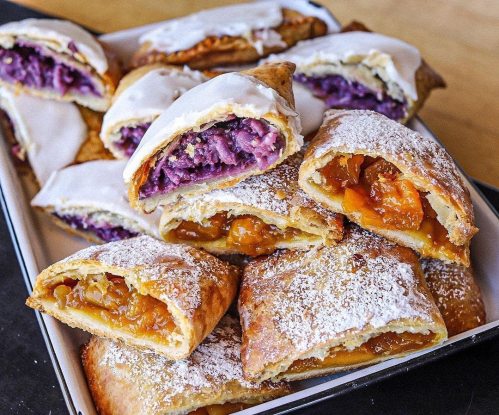 A platter of sweet pastries filled with purple and orange fruit, topped with icing and powdered sugar.