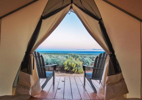 View from a tent entrance showcasing two chairs and a serene landscape with greenery and a distant horizon.