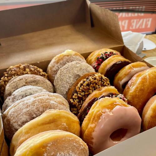 A box filled with assorted donuts, featuring various toppings and glazes, including sprinkles and nuts.