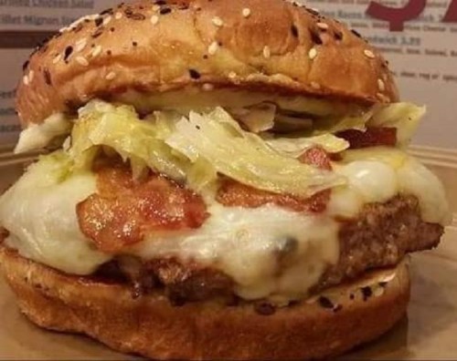A close-up of a sesame seed bun burger with lettuce, bacon, and melted cheese on a beef patty.