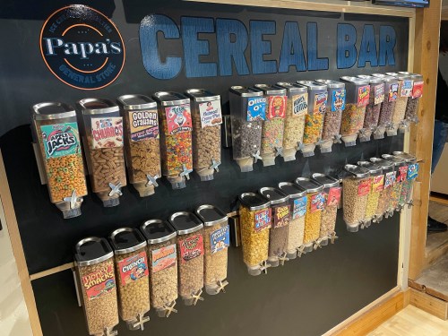 A colorful cereal bar display with various cereal types in clear containers, labeled with brand names.