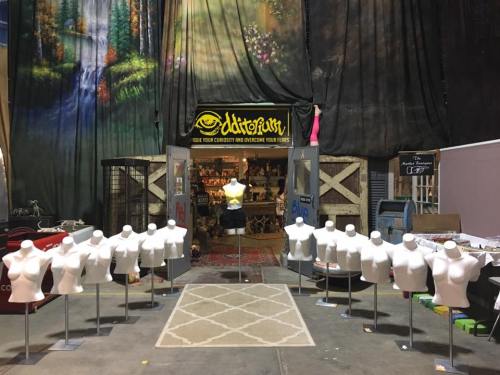 A display of white mannequins in front of a colorful backdrop and an entrance to a shop called "Oddity Rust."