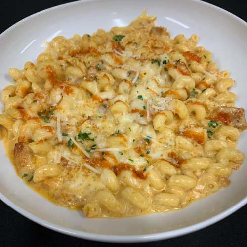A creamy pasta dish with curly noodles, topped with cheese, herbs, and a drizzle of sauce, served in a white bowl.