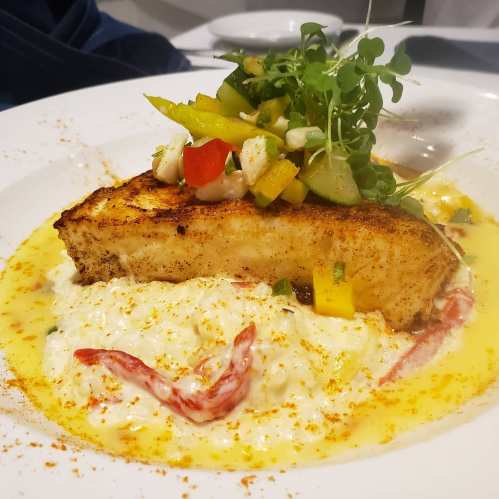 A beautifully plated dish featuring grilled fish topped with fresh salsa, served over creamy rice with colorful garnishes.