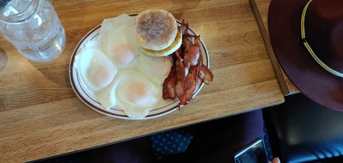 A plate with four fried eggs, crispy bacon, and a toasted English muffin on a wooden table.