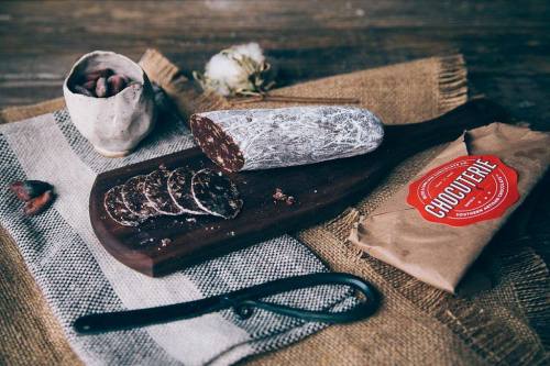A wooden board with sliced chocolate salami, a cup of cocoa beans, and a wrapped package labeled "Chocolaterie."