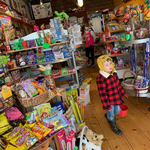 A child in a plaid jacket and hat walks through a colorful candy store filled with various sweets and treats.