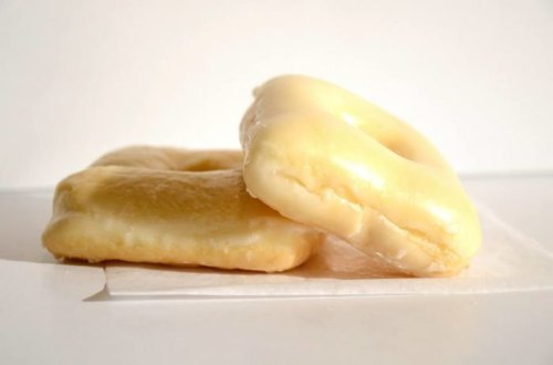 Two glazed donuts stacked on a white surface, with a light background.