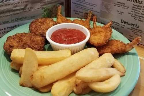 A plate of fried shrimp, hush puppies, and fries served with a side of marinara sauce.