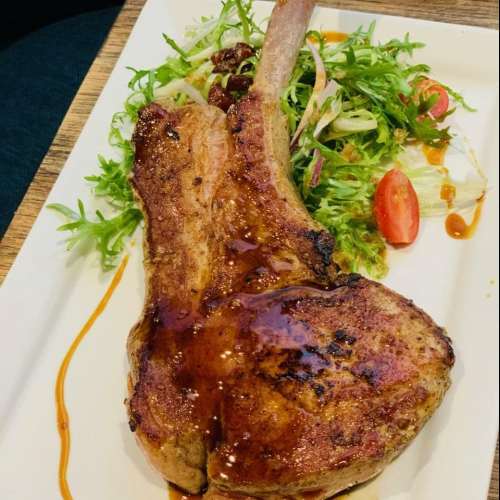 A juicy grilled pork chop served with a fresh salad and drizzled with sauce on a white plate.