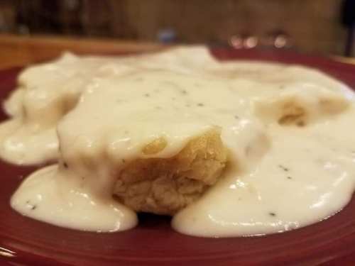 A close-up of a plate with biscuits smothered in creamy white gravy.
