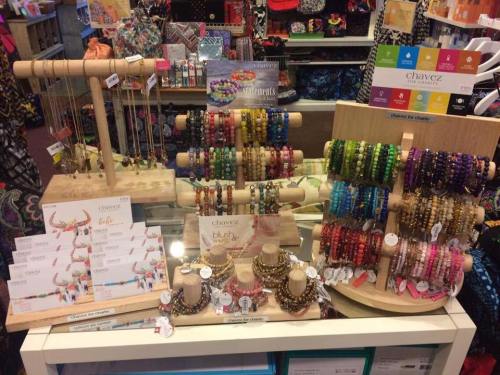 Display of colorful jewelry, including necklaces and bracelets, arranged on wooden stands in a retail store.