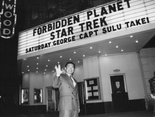 A man in a suit stands in front of a theater marquee displaying "Forbidden Planet" and "Star Trek."