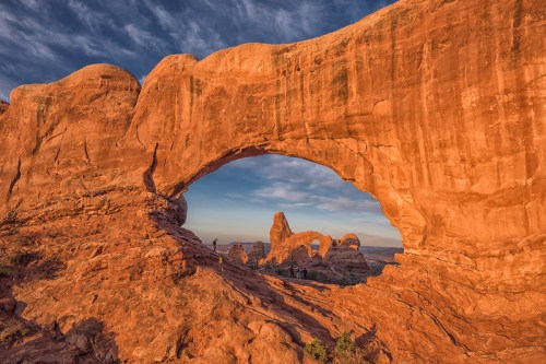 A stunning rock arch frames a scenic view of red rock formations under a colorful sky at sunset.