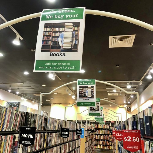 A bookstore interior with signs promoting book buying and green practices, surrounded by shelves of books and DVDs.