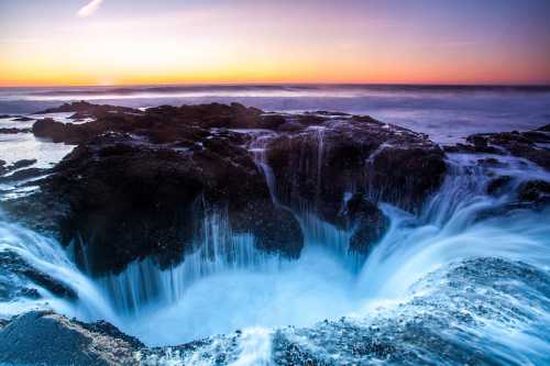 A dramatic coastal scene featuring a circular rock formation with cascading water at sunset, creating a serene atmosphere.