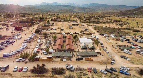 Aerial view of a desert area with tents, vehicles, and mountains in the background, showcasing a gathering or event.