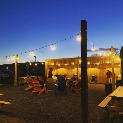 Outdoor gathering space at dusk, featuring string lights, colorful chairs, and people enjoying the atmosphere.