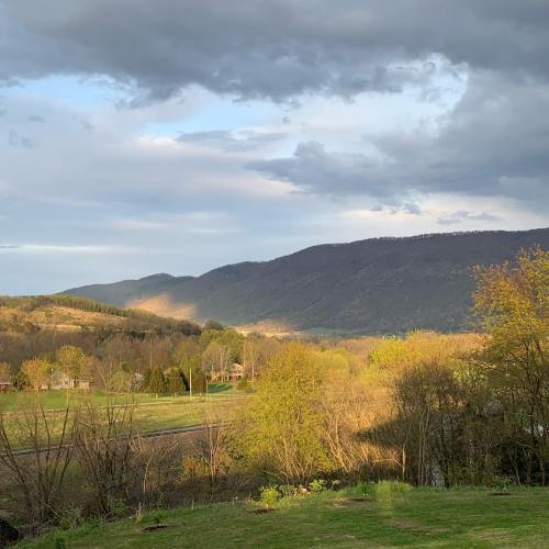 A scenic view of rolling hills and mountains under a partly cloudy sky, with green trees and fields in the foreground.