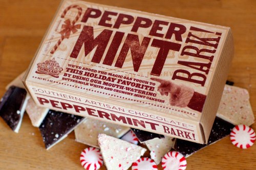 A box of peppermint bark with festive packaging, surrounded by pieces of bark and peppermint candies.