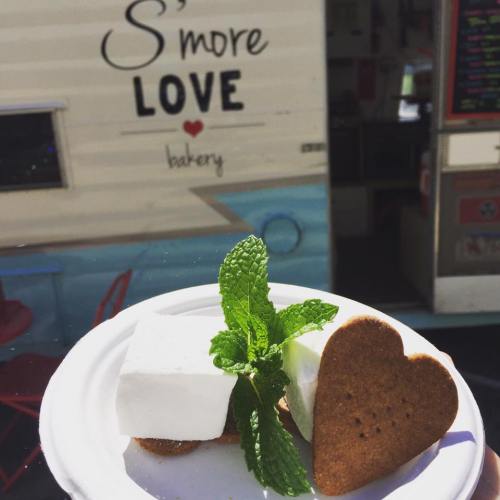 A plate with s'mores: a marshmallow, a heart-shaped cookie, and a mint leaf, with a bakery food truck in the background.