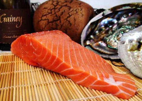 Fresh salmon fillet on a bamboo mat, surrounded by shells and a bottle of wine.