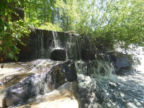A serene waterfall cascading over rocky terrain, surrounded by lush greenery and sunlight filtering through the trees.