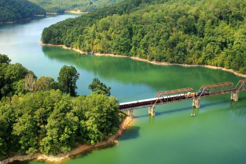 Aerial view of a bridge over a serene lake, surrounded by lush green trees and hills.