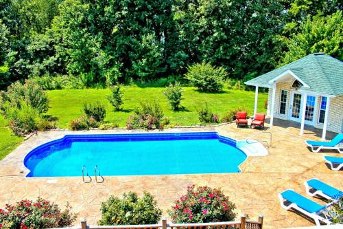 A bright blue swimming pool surrounded by lush greenery and colorful flowers, with lounge chairs and a gazebo nearby.