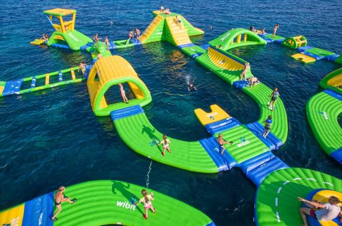 A vibrant inflatable water park with slides and obstacles, filled with people enjoying the sunny day on the water.