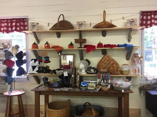 A cozy shop display featuring handmade crafts, baskets, hats, and colorful decorations on wooden shelves and a table.