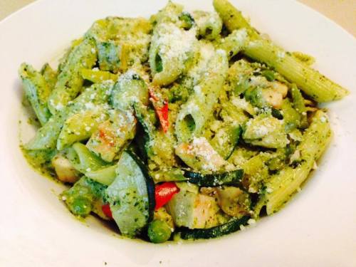 A bowl of penne pasta mixed with vegetables and pesto sauce, topped with grated cheese.