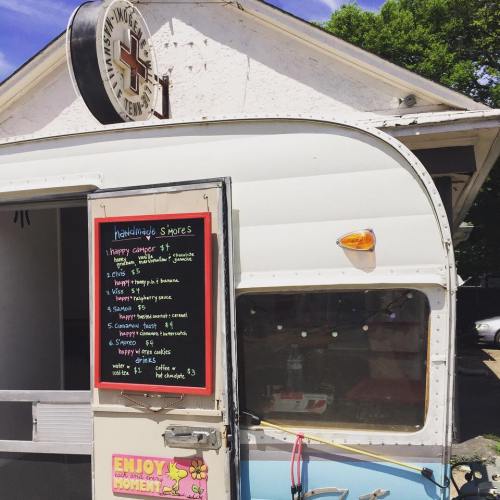 A food truck with a menu board featuring handmade s'mores and other treats, set against a sunny outdoor backdrop.