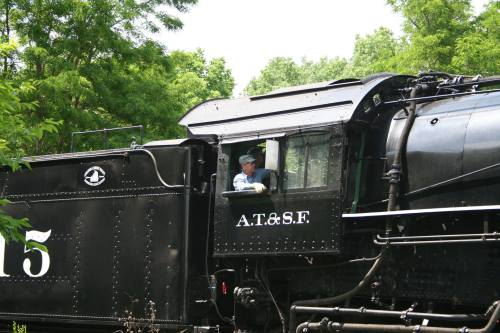 A vintage black steam locomotive with "A.T.&S.F." on the side, featuring an engineer in the cab.