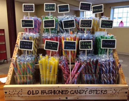 A display of colorful old-fashioned candy sticks in various flavors, labeled on small chalkboard signs.