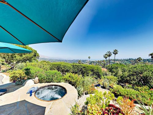 A scenic view from a patio with a hot tub, surrounded by lush greenery and palm trees under a clear blue sky.