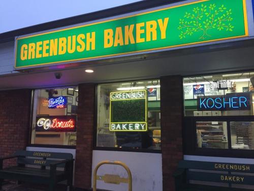 Exterior of Greenbush Bakery with neon signs for donuts and kosher items, featuring a bright green and yellow facade.