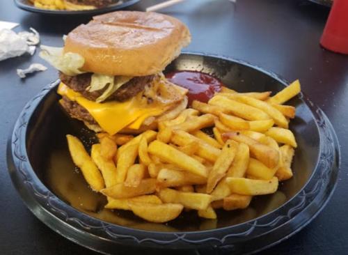 A plate with a cheeseburger topped with lettuce and two patties, accompanied by a side of golden fries and ketchup.