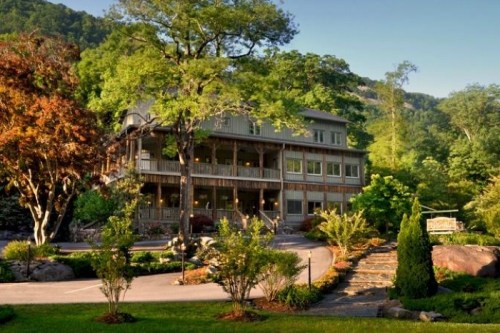 A charming lodge surrounded by lush greenery and trees, set against a backdrop of mountains.