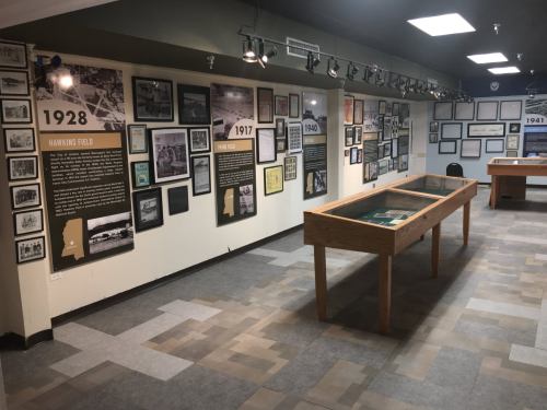 A museum exhibit featuring historical photos and information on walls, with display cases and seating in the background.
