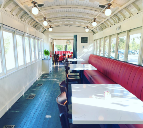 Interior of a diner with red booths, white tables, and large windows, featuring a bright and airy atmosphere.