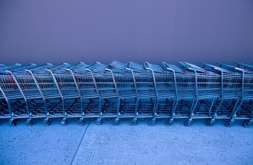 A row of metallic shopping carts lined up against a purple wall, creating a visually striking pattern.