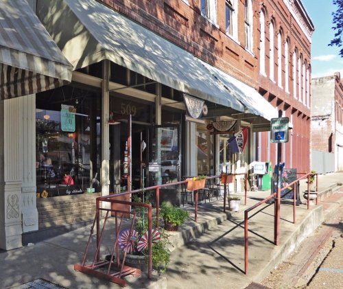 A charming storefront with large windows, awnings, and decorative elements, set on a historic brick street.