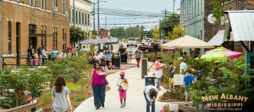 A lively street scene in New Albany, Mississippi, with people walking, shopping, and enjoying the outdoors.