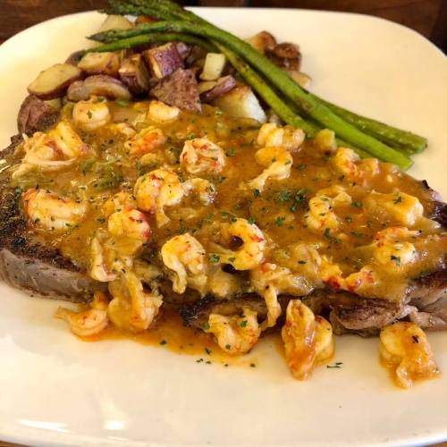 A plate featuring a grilled steak topped with shrimp sauce, served with red potatoes and asparagus.