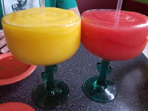Two colorful frozen drinks in cactus-shaped glasses: one yellow mango and one red strawberry.