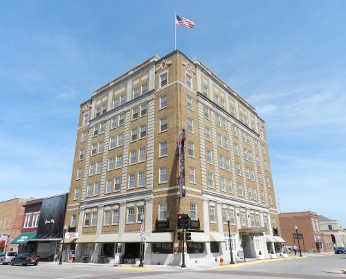 Historic brick building with an American flag, featuring multiple stories and a corner view in a small town.