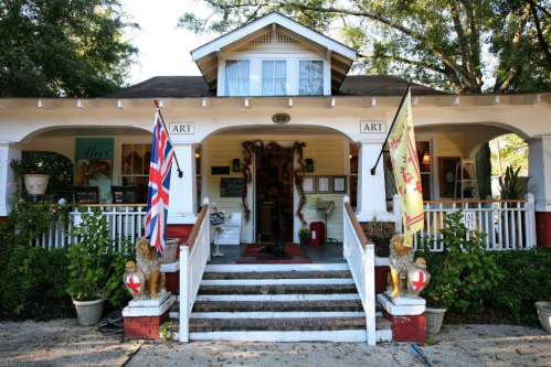 Charming art gallery with British flags, lion statues, and a welcoming porch surrounded by greenery.