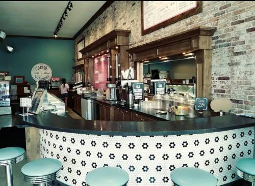 A cozy café interior featuring a service counter, vintage decor, and teal bar stools against a brick wall.