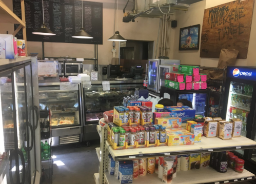 A small convenience store interior with shelves of drinks, snacks, and a display case for prepared foods.